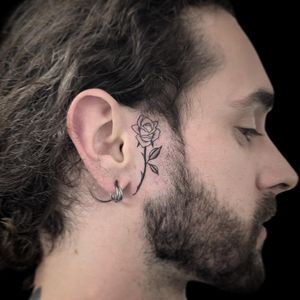 Elegant black and gray flower tattoo on the side of the face by Letitia Mortimer, featuring intricate fine line detailing.