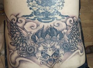 Avi's illustrative design features intricate filigree details on wings and a regal crown, creating a striking and elegant stomach tattoo.