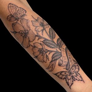 Explore the delicate beauty of black and gray dotwork with a design by Letitia Mortimer featuring a butterfly, flower, and leaf motif on your forearm.