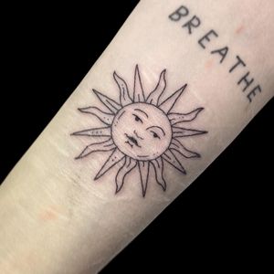 Elegant fine line sun motif tattoo on forearm, by Letitia Mortimer. Perfect for a subtle and stylish look.