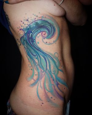 Experience the calming beauty of a watercolor wave tattoo on your ribs, expertly designed by Aygul.