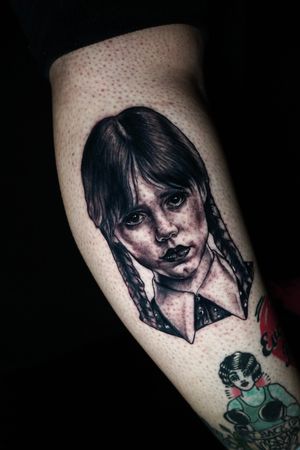 Stunning black and gray forearm tattoo of Wednesday Addams by the talented artist Miss Vampira. A perfect blend of realism and illustrative style.