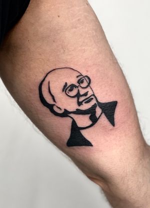 Capture the essence of a debonair man with glasses in this bold blackwork tattoo on your upper arm. Designed by the talented artist Miss Vampira.