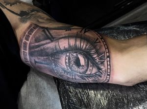 Incredible black and gray tattoo by Soheyl Astangi, featuring a detailed eye and clock design on the upper arm.
