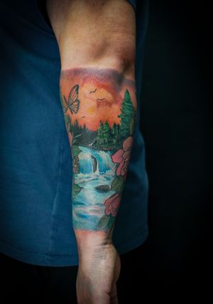 Vibrant tattoo by Soheyl Astangi featuring a stunning combination of a river, waterfall, and intricate flower design on the forearm.