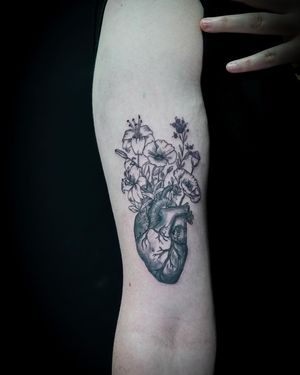 Elegant and realistic black and gray fine line tattoo of a delicate floral heart design, expertly crafted by Soheyl Astangi on the upper arm.