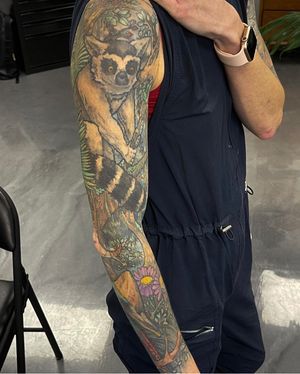 A stunning sleeve tattoo featuring a tree, flower, and lemur, expertly done by Gifford Kasen.