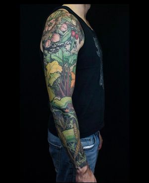 A stunning sleeve tattoo by Gifford Kasen featuring intricate floral motifs like flowers, fruits, leaves, and wheat.