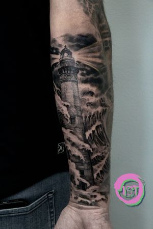 Detailed black and gray forearm tattoo featuring a realistic lighthouse surrounded by crashing waves. By artist Gifford Kasen.