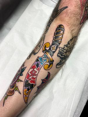 Stunning arm tattoo featuring a colorful neo traditional design of a flower and dagger by the talented artist Adam Ruff.