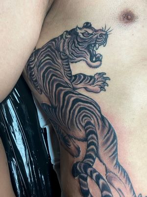 Experience the fierce beauty of a traditional black and gray tiger tattoo on your ribs by Adam Ruff.