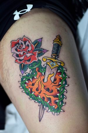 Beautiful traditional style tattoo featuring a rose and dagger design on the upper leg, done by the talented artist Adam Ruff.