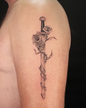 Embrace the beauty of a rose intertwined with a majestic sword on your upper arm. By José.