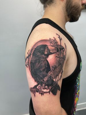 Embrace the magic of the night with this stunning blackwork tattoo on your upper arm. Featuring a realistic moon, bird, crow, raven, and tree by Gifford Kasen.