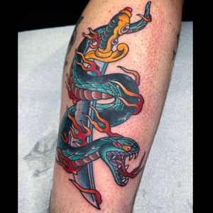 Get inked with this bold traditional tattoo featuring a menacing snake wrapped around a sharp sword, done by the talented artist Carlos Zucato.
