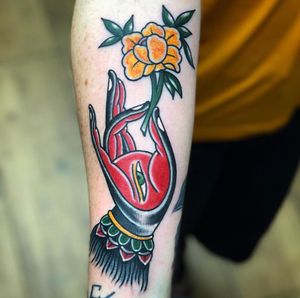 Stunning forearm tattoo by Carlos Zucato featuring a beautiful traditional design of a flower and hand. Bold colors and intricate details bring this piece to life.
