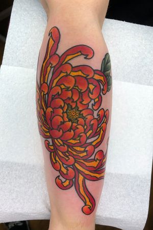 Experience the beauty of a traditional Japanese chrysanthemum tattoo expertly crafted by Carlos Zucato on your lower leg.