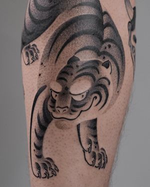 Black and gray illustrative tattoo of a fierce tiger by FKM TATTOO on lower leg.