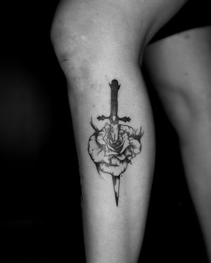 Stunning black and gray tattoo of a delicate rose intertwined with a sharp knife, expertly done by Jeff Huet on the lower leg.