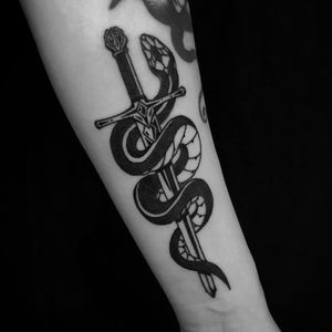 Bold blackwork design by Jeff Huet featuring a striking snake and dagger motif on the forearm.