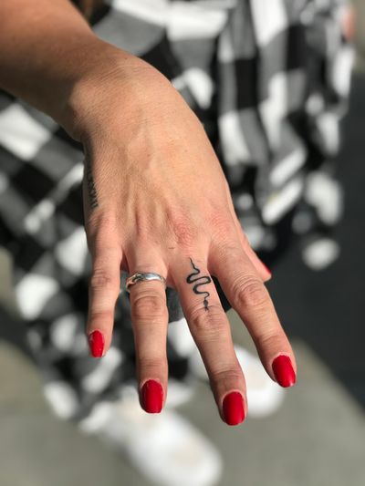 Elegant and intricate fine line snake tattoo on finger, expertly done by renowned artist Jeff Huet. A sleek and unique design for a bold statement.