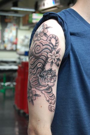 Breathtaking upper arm tattoo featuring a fierce tiger and delicate flower in Bananajims' signature dotwork Japanese style.