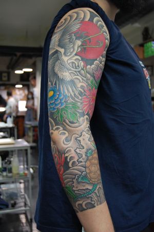 Experience the beauty of traditional Japanese art with a stunning sleeve tattoo featuring intricate flower and heron motifs, masterfully crafted by Bananajims.