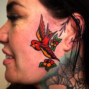 Get inked by Alessandro Lanzafame with a stunning traditional bird design on your side face. Stand out with this unique tattoo!