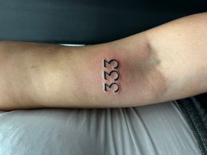 A unique upper arm tattoo featuring small lettering of a number and quote, designed by Misa.
