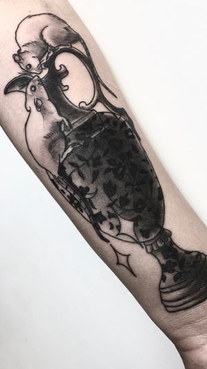 Get inked by Victor Martin with a unique black & gray design featuring a rat and a vase on your forearm.