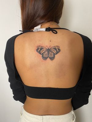 Elegant black and gray butterfly tattoo by Victor Martin, beautifully placed on the upper back for a timeless and classy look.