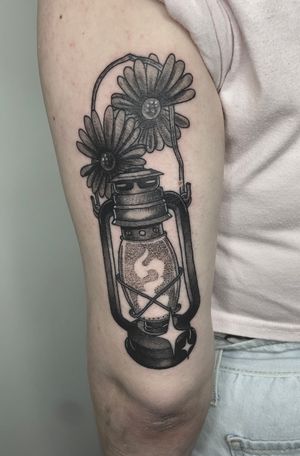 Victor Martin creates a stunning black and gray tattoo of a delicate flower and lantern motif on the upper arm.