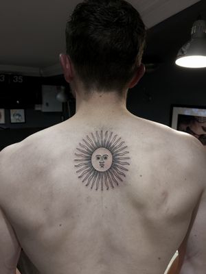 Get inked with a stunning fine line sun tattoo on your upper back by the talented artist Luca Salzano.