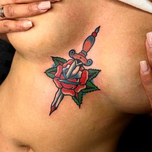 Get a stunning traditional tattoo featuring a beautiful flower and dagger motif by the talented artist Alessandro Lanzafame.