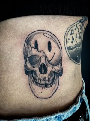 Unique dotwork and illustrative style tattoo featuring a skull with a smiley face, by talented artist Kat Jennings.