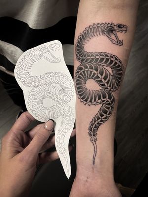 Get inked with a striking snake entwined around a skeleton by Kat Jennings. A unique and captivating design for tattoo enthusiasts.