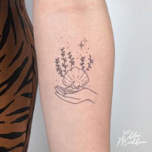 Experience the delicate artistry of Chloe Mickham with this stunning tattoo featuring a moon, shell, and hand design. Perfect for those seeking a stylish and unique body art masterpiece.