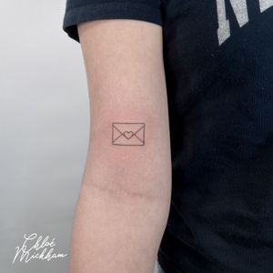 Get inked with a delicate fine line tattoo featuring an envelope and letter motif, symbolizing love and affection. Created by the talented Chloe Mickham.