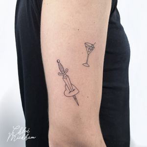 Exquisite fine line tattoo combining a dagger and a martini, created by the talented artist Chloe Mickham.