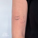 Elegant fine line tattoo featuring a minimal design of a nose and eye, by Chloe Mickham.