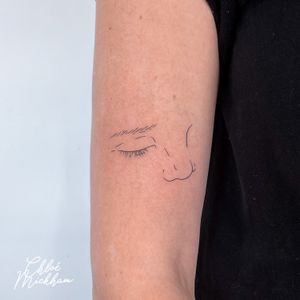 Elegant fine line tattoo featuring a minimal design of a nose and eye, by Chloe Mickham.