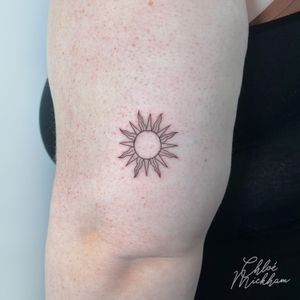 Get ready to bask in the beauty of this fine line, illustrative sun tattoo by Chloe Mickham. Radiate positivity with this stunning piece!