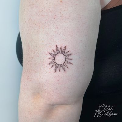 Get ready to bask in the beauty of this fine line, illustrative sun tattoo by Chloe Mickham. Radiate positivity with this stunning piece!