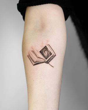 Get lost in the enchanting world of this micro realism tattoo featuring a fantasy book motif by the talented artist Viola.