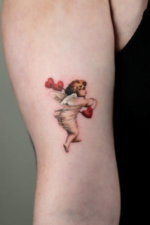 Get mesmerized by Viola's stunning micro-realism tattoo of an angel and cupid in vibrant colors.
