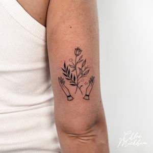 Elegant and intricate tattoo by Chloe Mickham featuring fine line illustration of flowers intertwined with hands.