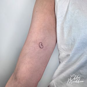 Elegant fine line tattoo of a simple bean motif, expertly executed by the talented artist Chloe Mickham.