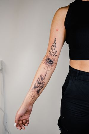 Explore the intricate details of this captivating black and gray geometric tattoo featuring a delicate hand and eye motif. By talented artist Gabriele Edu.