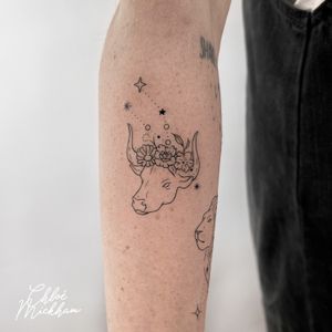 Get a unique and delicate fine line tattoo featuring a star, cow, and flower design by the talented artist Chloe Mickham.