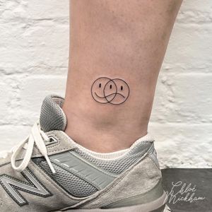 Express both sides of your emotions with this fine line tattoo by Chloe Mickham featuring a smiley and sad motif.